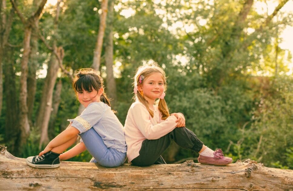 Two young girls sitting on a log in a forest. Naturopath for Children. Brisbane Livewell Clinic