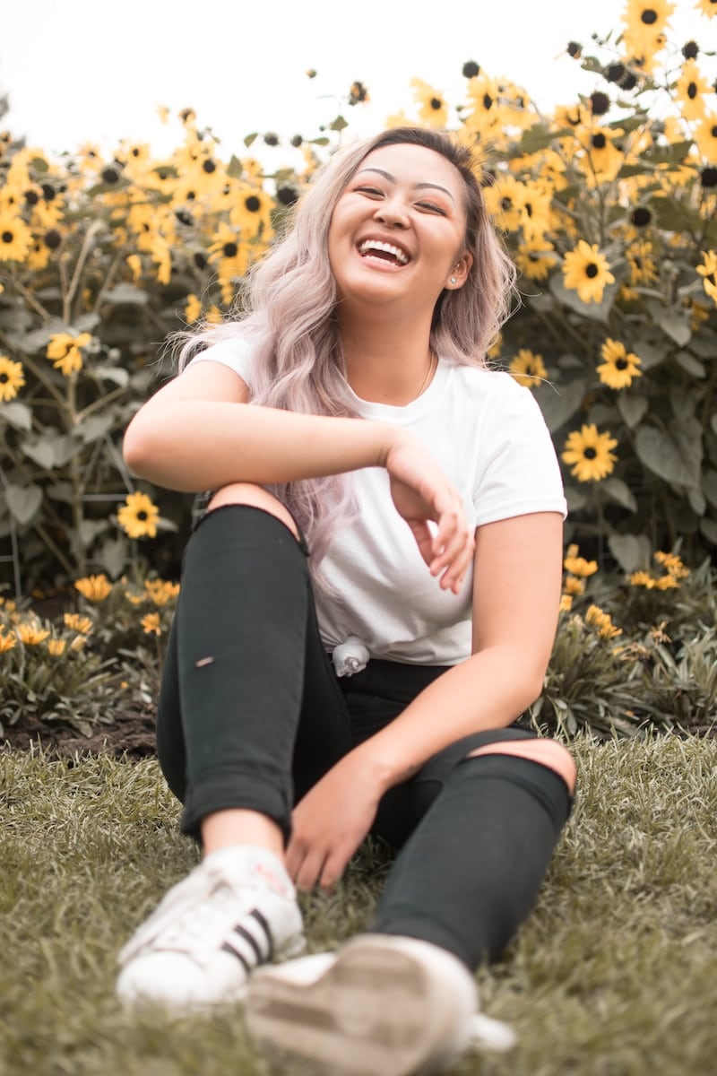 Woman laughing and sitting in front of sunflowers. Weight Gain and Digestive Problems - Brisbane Livewell Clinic